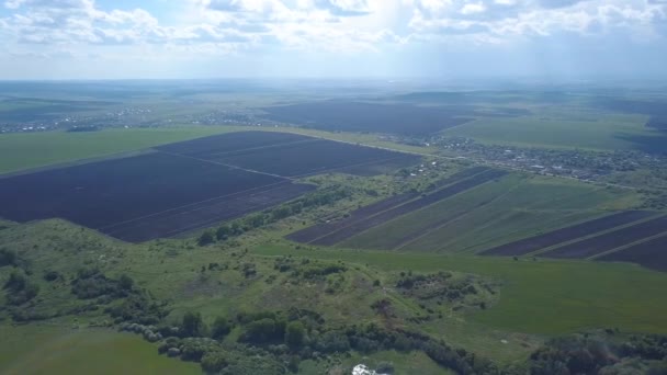 Aerial syn på plöjas och sått fält nära byn eller jordbrukare hus i soliga sommardag mot blå grumlig himmel. Klipp. Vacker utsikt över landskapet landskap — Stockvideo