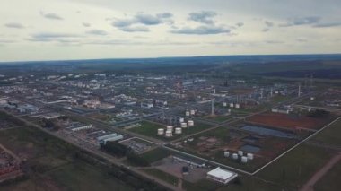 Bulutlu gökyüzüne karşı arka planda alanları ve ağaçları ile şehir dışında bulunan büyük sanayi bölgesinin yukarıdan görünümü. Klip. Fabrika tankları ve tank çiftliği inanılmaz görünümü.