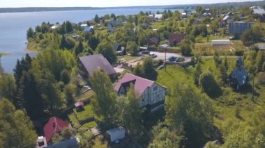 Yaz günü arka planda büyük nehir ile iğne yapraklı ve yaprak döken ağaçlarla çevrili yazlık köy ve evlerin görünümü. Klip. Pitoresk kırsal manzara güzel görünümü