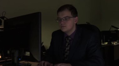 Erkek ofis çalışanı gece geç saatlerde laptopta gerekli bilgileri arıyor. Stok görüntüleri. Genç bir çalışan masasında oturmuş bilgisayarda yazı yazıyor..