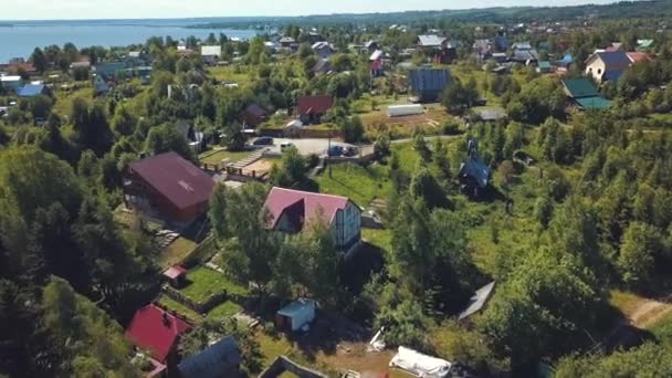 Vue du village de chalets et des maisons entourées de conifères et de feuillus avec la grande rivière en arrière-plan le jour d'été. Clip. Belle vue sur le paysage pittoresque de la campagne — Video