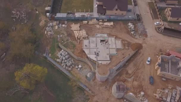 Vue aérienne du chantier en cours près du nouveau chalet moderne, des matériaux de construction et des travailleurs versant du béton pour la fondation. Clip. Processus de construction de nouveaux bâtiments .