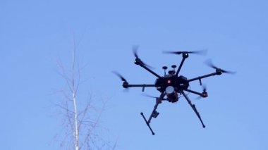 Görünür pervane hareketleri ve mavi gökyüzü arka planında yanıp sönen ışık ile uçan siyah kamera dronu. Şarjör. Mavi gökyüzüne karşı şasiyi serbest bırakan küçük bir kuadkopter..