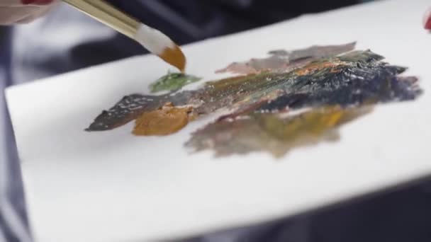 Close up de mão mulher segurando uma escova e uma paleta com tintas a óleo, conceito de arte fina. Acção. Mulher artista pinta um quadro de tinta a óleo com um pincel na mão, de perto . — Vídeo de Stock