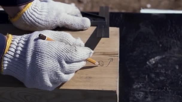 Nahaufnahme für die Hände eines Tischlers in Schutzhandschuhen, der etwas auf ein Holzbrett schreibt. Clip. Tischlerarbeiten, Messen und Markieren des Holz-, Holz- und Möbelbaukonzeptes. — Stockvideo