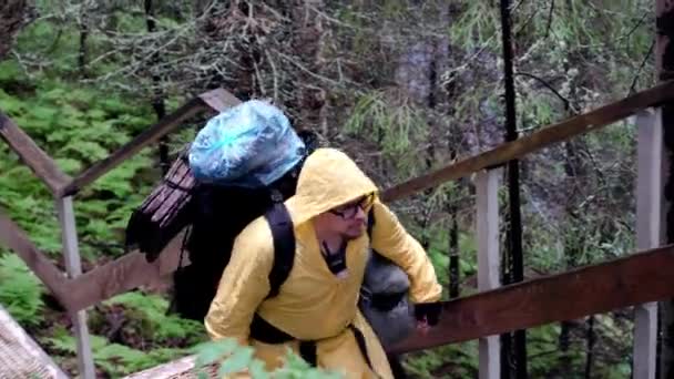 Исследователь в лесной кампании. Запись. Человек с огромным снаряжением и рюкзаками исследовать окружающую среду и поднимается по лестнице в лесу — стоковое видео