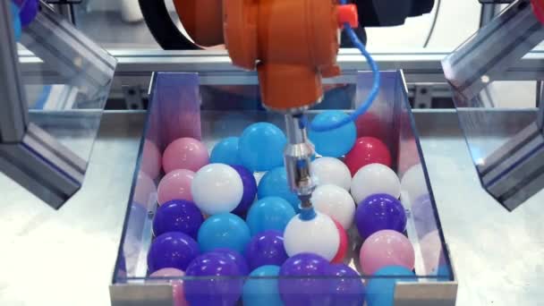 Gran mano robótica naranja reubicando pequeñas bolas multicolores de plástico de una sección a otra. Medios. Diferentes colecciones de robots de trabajo presentadas en la exposición foro de robótica — Vídeo de stock