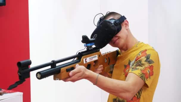 Close-up of man holding a weapon and shooting in virtual reality on the exhibition. Media. Electronic devices and mechanisms are presented at the scientific exhibition. — Stock Video