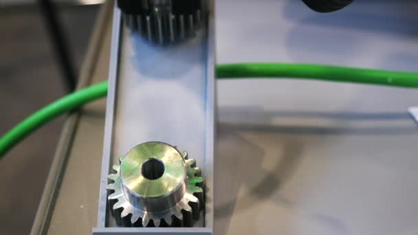 Zbliżenie małego metalu biegu leżącego na stole w pobliżu automatycznego urządzenia robotycznego. Media. Urządzenia elektroniczne i mechanizmy są prezentowane na wystawie naukowej. — Wideo stockowe