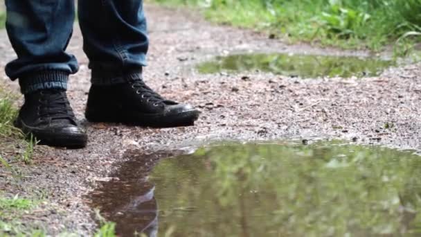 森の小道の水たまりで男のクローズアップ。ストック映像。水たまりに立ち、行き方を考える人の足の眺め — ストック動画