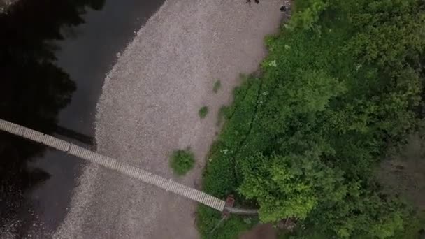 Top view of bridge passing through river in forest. Stock footage. Suspended wooden bridge passes through wide river in forest area — Stock Video