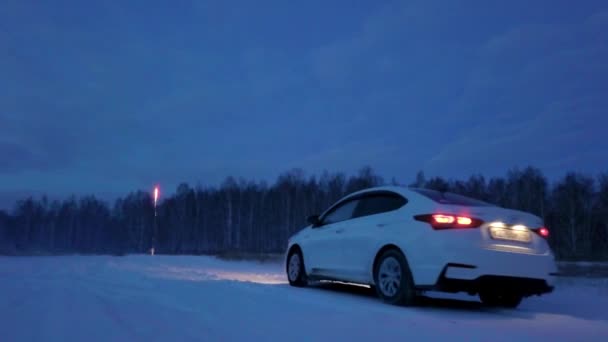 Bil på vintern väg nära skogen på kvällen. Stock film. Utsikt från bak i bilen på snötäckta vägen nära Forest Strip i slutet av kvällen. Bil går till skogen på bakgrunden av fyrverkerier — Stockvideo