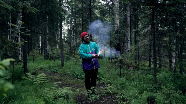 Homem com bombas de fumo coloridas na natureza. Imagens de stock. Jovem incendiou bombas de fumo e elas brilhavam antes da fumaça na floresta — Fotografia de Stock