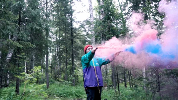 Man and colored smoke bombs in forest. Stock footage. Young man lit smoke colored checkers in forest for beautiful photography