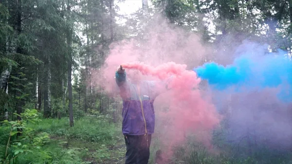 Man and colored smoke bombs in forest. Stock footage. Young man lit smoke colored checkers in forest for beautiful photography