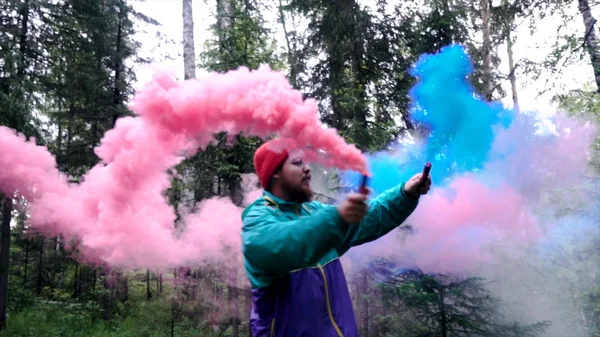 Uomo con bombe fumogene colorate in natura. Filmati delle scorte. Giovane uomo diffonde ruscelli di controllori di fumo colorati nella fitta foresta — Foto Stock