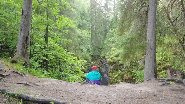 Homem sentado na floresta caído rocha. Imagens de stock. Viajante jovem olha para o colapso assustador na paisagem rochosa da floresta densa — Fotografia de Stock