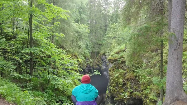 Mann sitzt im Wald umgestürzte Felsen. Archivmaterial. junger Reisender sieht beängstigenden Einsturz in felsiger Landschaft mit dichtem Wald — Stockfoto