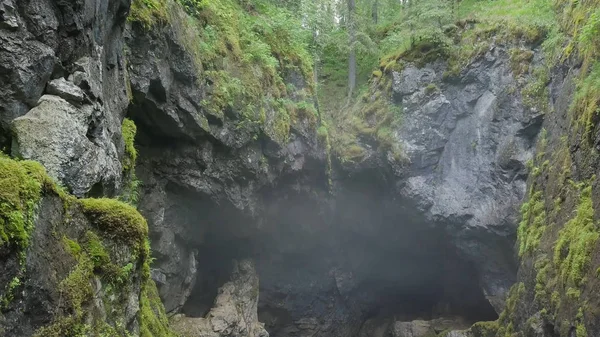 Top view of gorge between rocks in forest. Stock footage. Two cliffs covered with moss hang over small gorge with fog on background of forest. Gorge suggestive fear your mystical haze