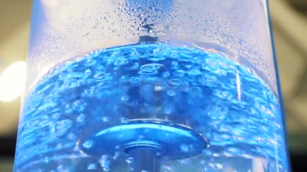 Acqua bollente in grande refrigeratore di vetro con retroilluminazione al neon e tubo metallico. I media. Vista ravvicinata dell'acqua più pura nel dispositivo di raffreddamento con le bolle è illuminato con luce colorata — Video Stock
