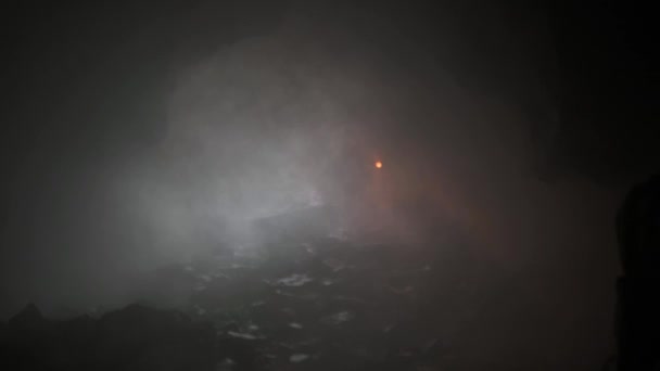 Viajero con antorcha en cueva oscura. Imágenes de archivo. El hombre con antorcha es seleccionado de la oscura cueva brumosa. La silueta del hombre con la antorcha débil sube sobre las piedras hasta la cima en la oscuridad de tono de la cueva — Vídeos de Stock