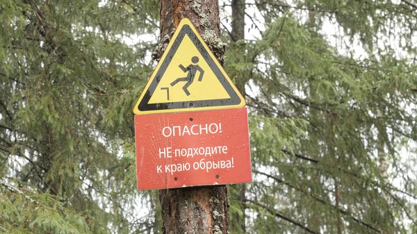 Danger sign of man falling from cliff. Stock footage. Sign hanging from tree warns tourists about cliff in coniferous forest. Sign with falling man with warning caption about cliff