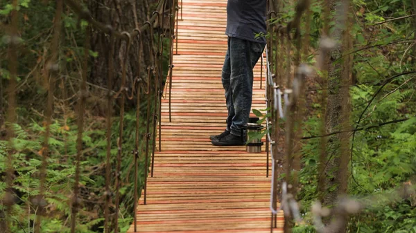 El viajero disfruta de vistas mientras está de pie en el puente colgante. Imágenes de archivo. El hombre se detuvo en un puente de madera para admirar la belleza de la naturaleza. Hombre fumar pipa mientras disfruta de la naturaleza — Foto de Stock