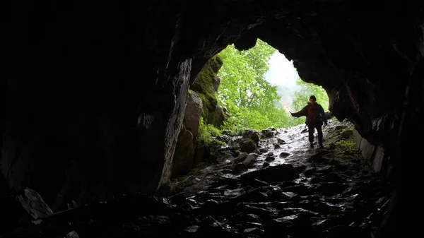 Wandelaar naar beneden in grot. Stock footage. Reiziger met rode signaal kaars daalt in grot op helling op achtergrond van gewelfde ingang — Stockfoto
