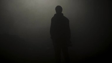 Dumanlı karanlıkta duran adamın siyah silueti. Stok görüntüleri. Genç adamın gizemli silueti karanlıkta duruyor sadece sis loş ışıkla aydınlatılmış