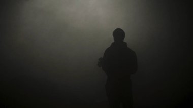 Dumanlı karanlıkta duran adamın siyah silueti. Stok görüntüleri. Genç adamın gizemli silueti karanlıkta duruyor sadece sis loş ışıkla aydınlatılmış
