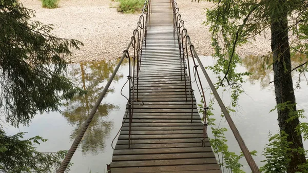 Wooden bridge suspended over forest river. Stock footage. Old hanging wooden bridge over which travelers are afraid to cross