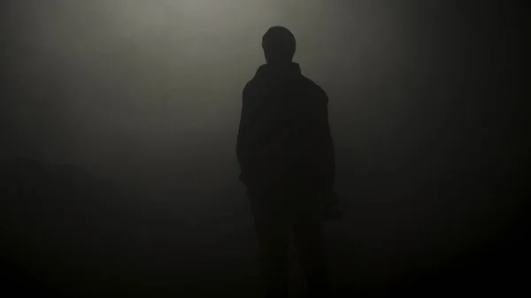 Dumanlı karanlıkta duran adamın siyah silueti. Stok görüntüleri. Genç adamın gizemli silueti karanlıkta duruyor sadece sis loş ışıkla aydınlatılmış