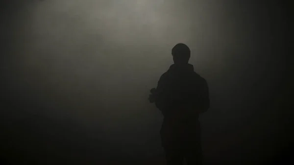 Μαύρη σιλουέτα του ανθρώπου που στέκεται σε σκούρο σκοτάδι. Υλικό από μετοχές. Μυστηριώδης σιλουέτα του νεαρού ανθρώπου στέκεται στο σκοτάδι φωτίζεται μόνο από αμυδρό φως στην ομίχλη — Φωτογραφία Αρχείου