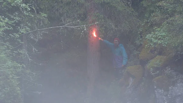 Fuoco rosso. Filmati delle scorte. L'escursionista si è perso nel bosco durante l'escursione e ora sta agitando il rosso. Le onde del viaggiatore segnalano il fuoco lasciando molto fumo nella foresta oscura — Foto Stock