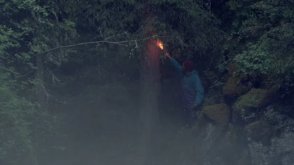 Red signal fire. Stock footage. Hiker got lost in woods during hike and now hes waving red flare. Traveler waves signal fire leaving lot of smoke in dark forest