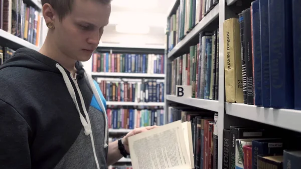 Young student is looking for book in library. Stock footage. Hipster student is looking for book to report in library. Young man takes book in library reads couple of lines and puts it back
