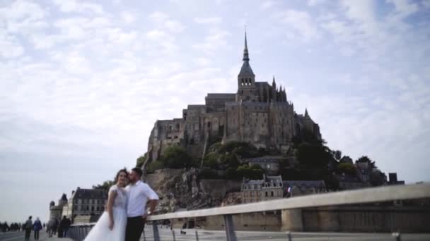 Sposi su sfondo di vecchio castello su collina su sfondo di cielo. Azione. Bella giovane coppia in abiti da sposa stare sullo sfondo del castello medievale — Video Stock