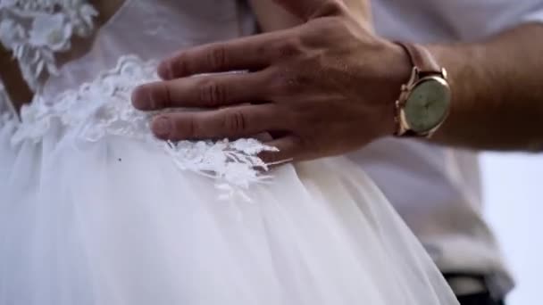 Close-up de maridos mãos abraçando esposa. Acção. Marido toca suavemente a cintura de suas esposas em vestido de noiva branco. Conceito de casamento — Vídeo de Stock