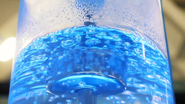 Boiling water in large glass cooler with a neon backlight and metal tube. Media. Close-up view of purest water in cooler with bubbles is illuminated with colorful light