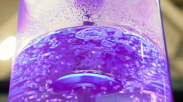 Boiling water in large glass cooler with a neon backlight and metal tube. Media. Close-up view of purest water in cooler with bubbles is illuminated with colorful light