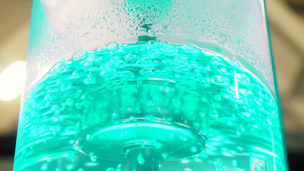 Boiling water in large glass cooler with a neon backlight and metal tube. Media. Close-up view of purest water in cooler with bubbles is illuminated with colorful light