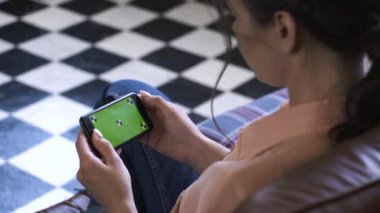 Pembe gömlekli genç kadının akıllı telefonunu yatay olarak tutarak hroma anahtar yeşil ekrana dokunduğu yakın çekim. Stok görüntüleri. Kendi içeriğinizin yerleştirilmesi için Renk anahtar ekranı.