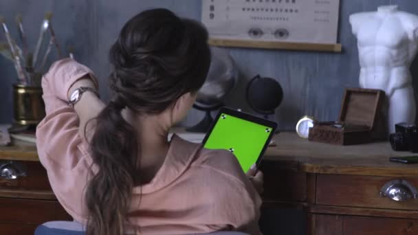 Vista desde la parte posterior de la niña bonita sentada en la mesa y el uso de la tableta de ordenador con croma pantalla verde clave. Imágenes de archivo. Pantalla de clave de croma para la colocación de su propio contenido . — Vídeos de Stock