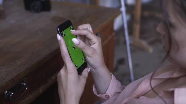 Vista dalla spalla di giovane donna in camicia rosa con capelli scuri che digita sul suo smartphone con schermo verde chroma key. Filmati delle scorte. Smartphone nuovo concetto di tecnologia — Video Stock