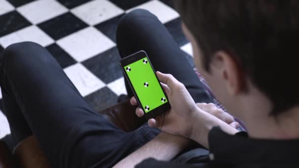 Vista do ombro do homem em camisa preta e jeans segurando um smartphone na mão e tocando na tela por dedo no modo retrato com tela verde. Imagens de stock. Tela verde chave Chroma — Vídeo de Stock