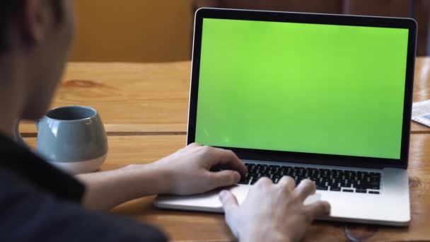Vista da parte de trás do homem de camisa preta sentado à mesa e digitando no laptop com tela de tecla croma verde. Imagens de stock. Laptop novo conceito de tecnologia, tela verde chave chroma — Vídeo de Stock