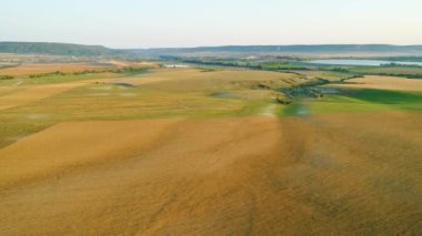 Tepelerin ve köylerin arka planında sarı kırsal alanların üst görünümü. Atış. Küçük gölün arka planında tarım alanları peyzaj ve köyün ufukta yer