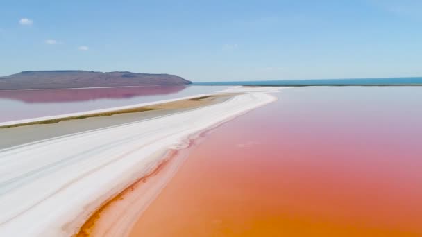 Orangensee auf der Krim. Schuss. Blick von oben auf leuchtend orangefarbenes Seewasser gegen weißen Sand. Außerirdische Landschaft aus farbenfrohem orangefarbenem Wasser auf weißem Sand vor blauem Himmel — Stockvideo