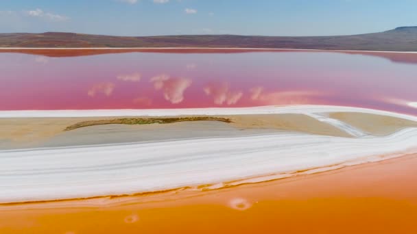 Blick von oben auf Wolken, die sich in rosa See spiegeln. Schuss. leuchtend bunte orangefarbene und rosa Seen sind durch weiße Ufer getrennt. schöne Reflexion von Wolken und blauem Himmel in rosa See — Stockvideo