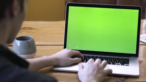 Вид со спины человека в черной рубашке, сидящего за столом и сидящего на ноутбуке с экраном с зеленой хромированной клавишей. Запись. Ноутбук новая концепция технологии, хрома ключ зеленый экран — стоковое видео